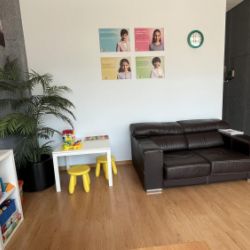 Detalle de sala de espera con sofá marrón grande y rincón de mesa y juegos infantiles